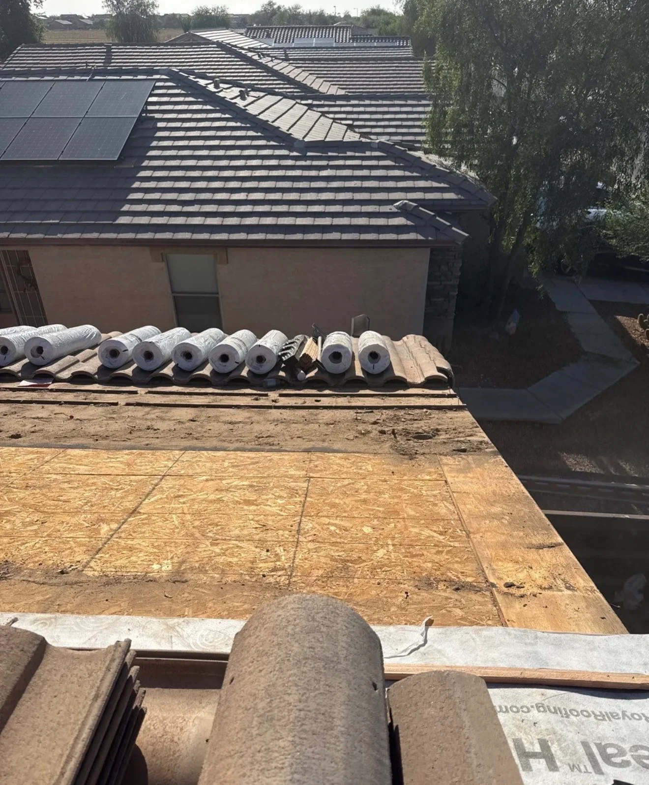 Slate roof installation with underlayment rolls and materials staged on residential property