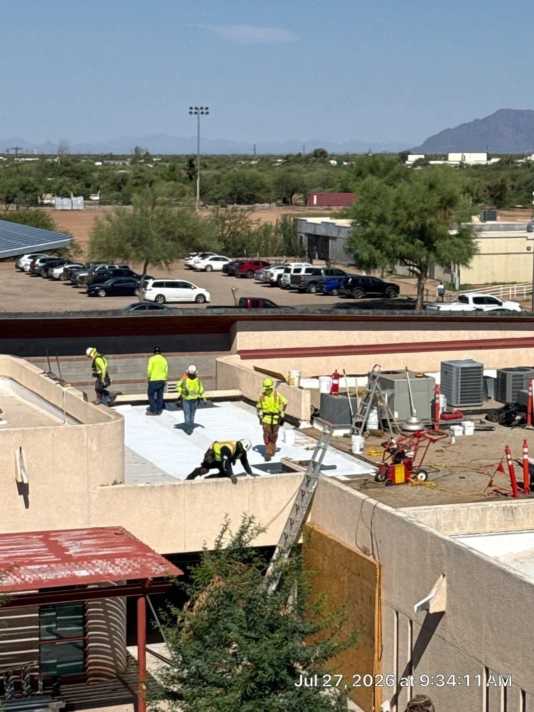 Crew installing white TPO membrane on commercial flat roof with safety equipment and staging