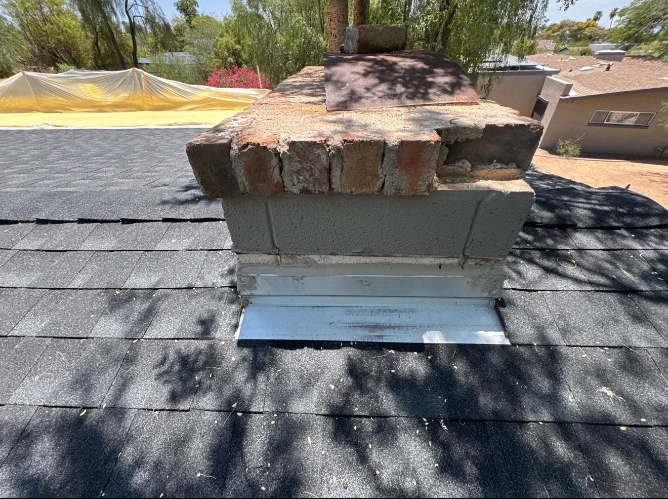 Metal flashing installed around brick chimney on asphalt shingle roof with protective covering visible