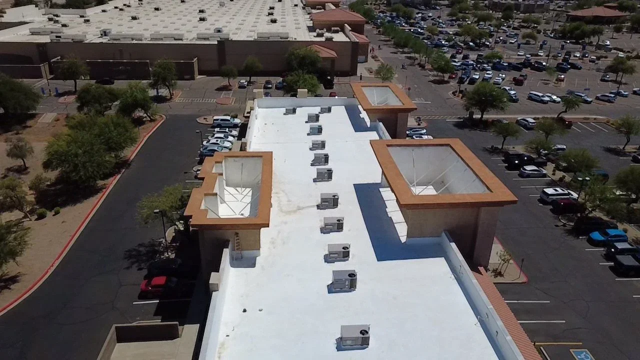 Aerial view of white flat roof with HVAC units, copper skylights, and blue accent stripe on commercial building