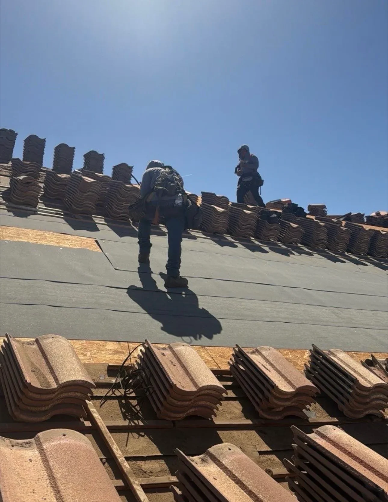 Clay barrel tile roof installation with workers positioning tiles on pitched roof structure