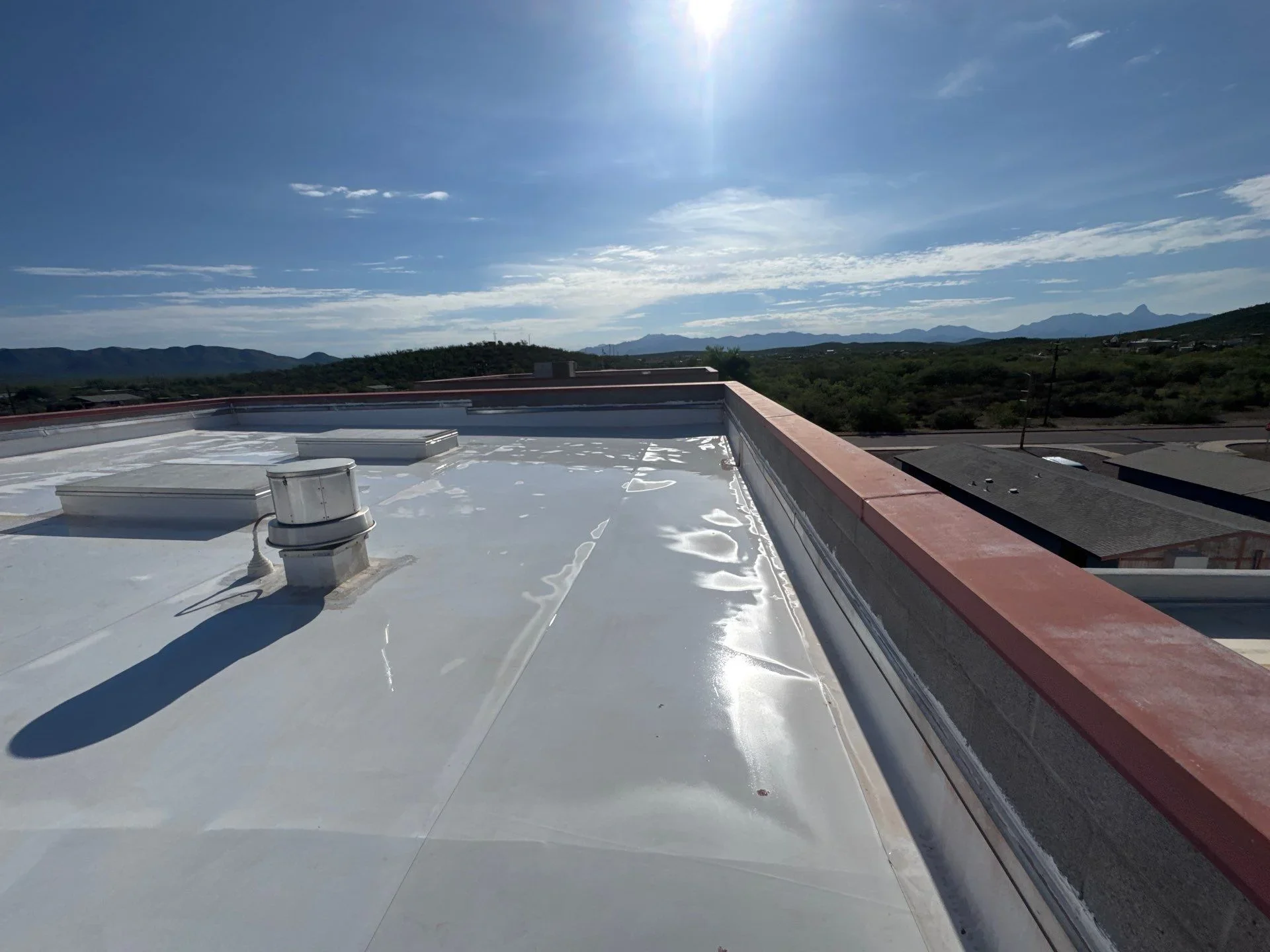 White membrane flat roof with metal flashing, vents, and parapet edge on commercial building