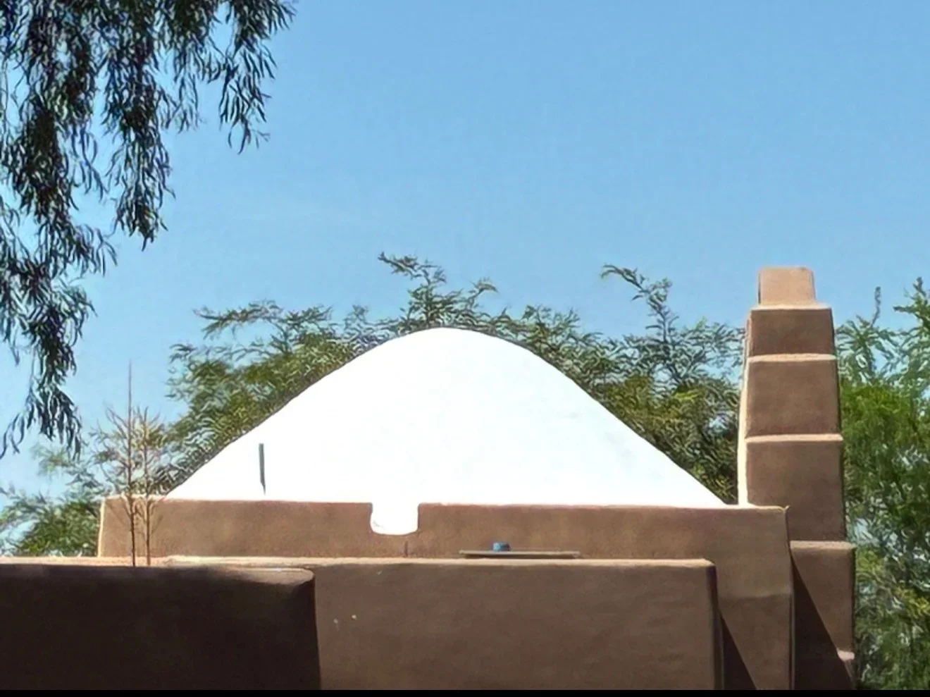 White dome roof with brick chimney on stucco walls, clear sky background
