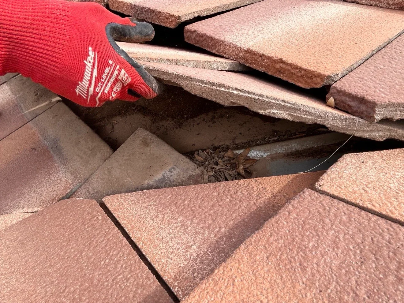 Worker in red gloves removing debris from between clay roof tiles during inspection