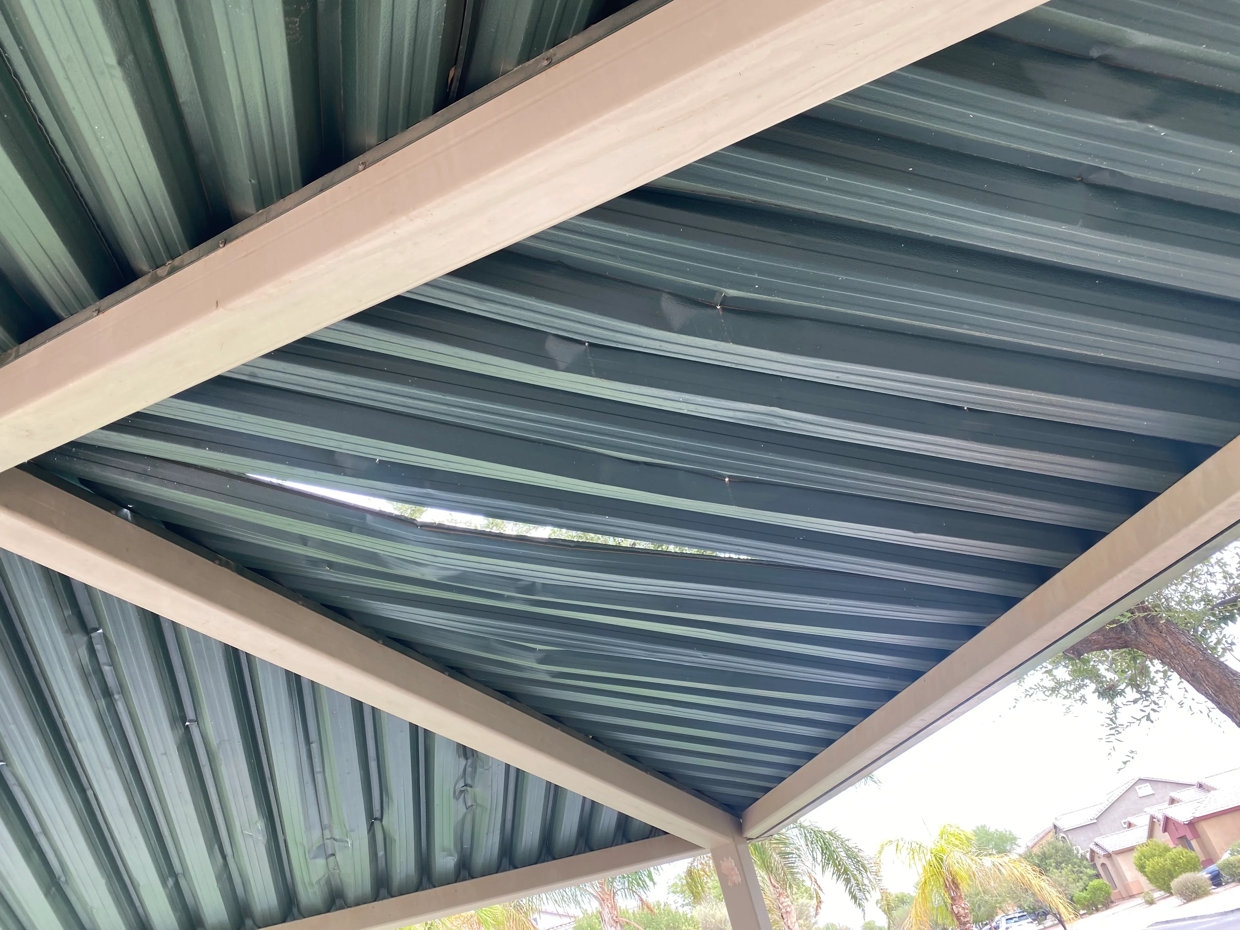 Dark corrugated metal roof panels installed on structural beams with tan trim framing