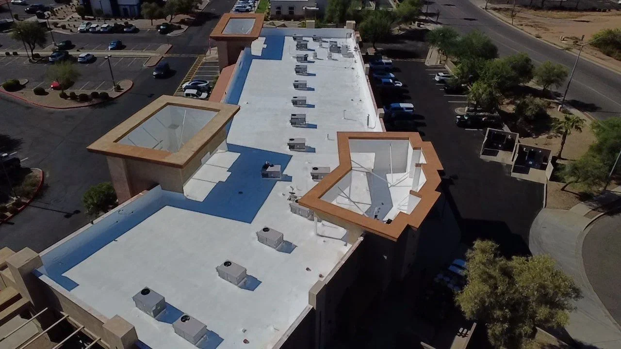 Aerial view of flat roof with white TPO membrane, blue trim, HVAC units, and copper-framed skylights