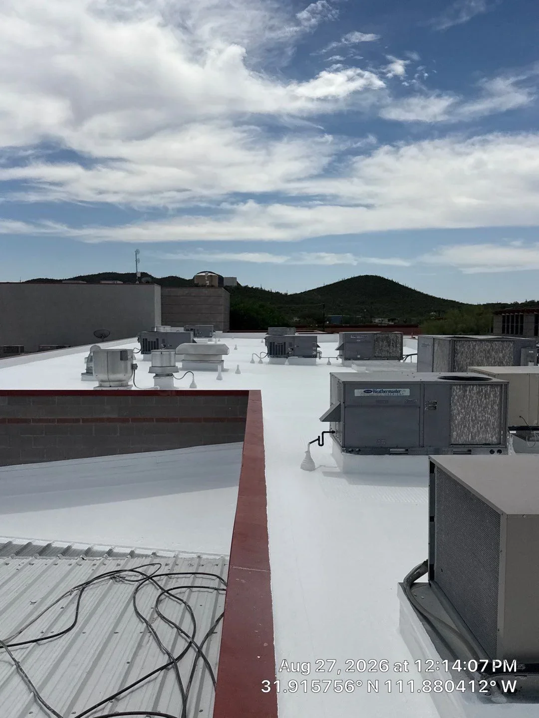 White membrane flat roof with HVAC units, metal flashing, and red trim on commercial building
