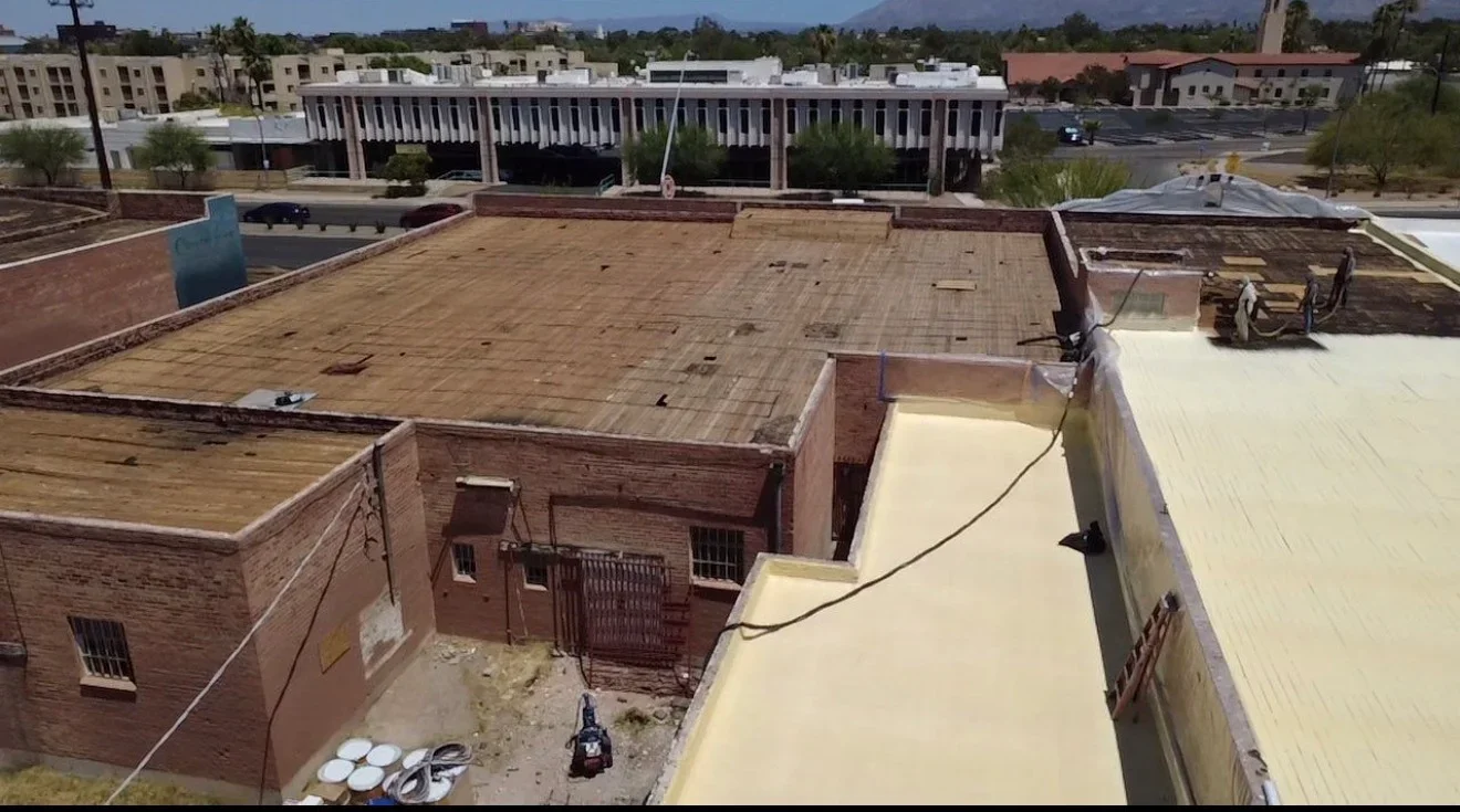 Commercial flat roof with new light coating applied to sections, brick parapet walls, and roof deck preparation in progress