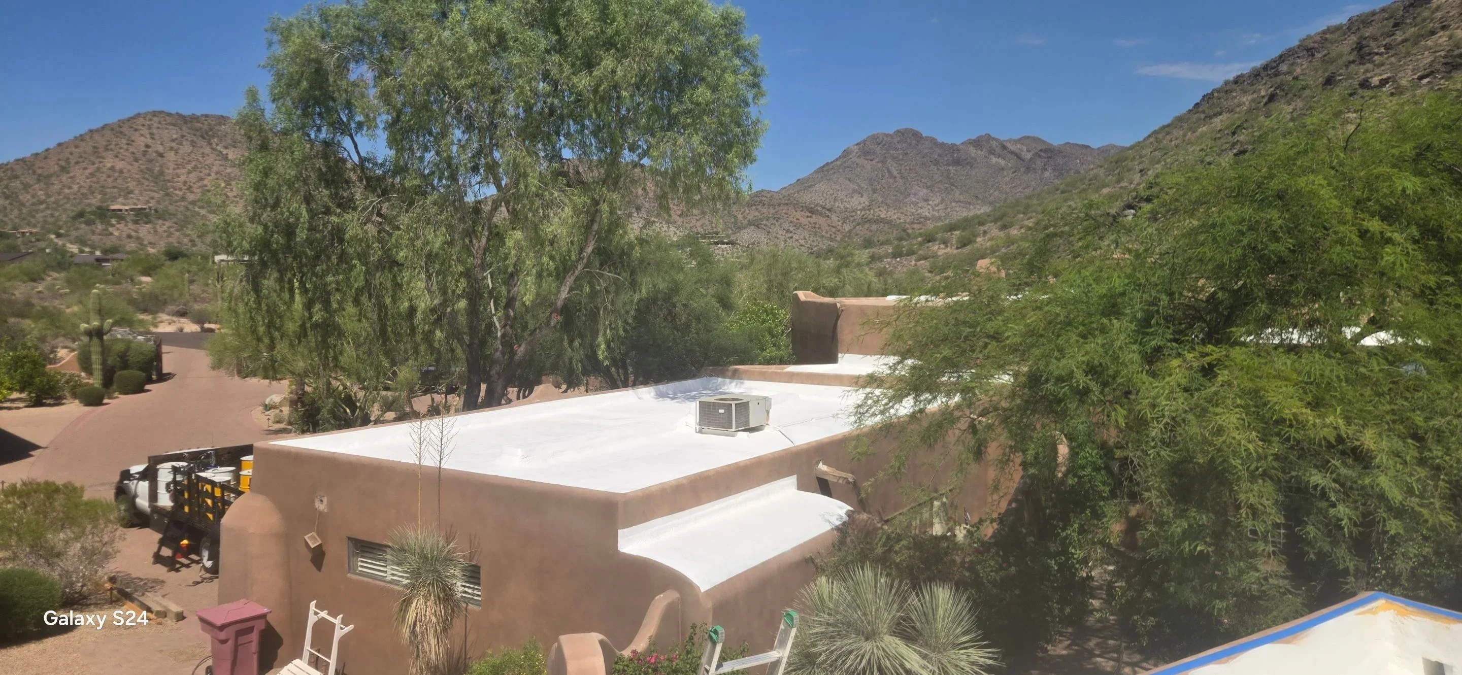 White membrane flat roof installation on adobe home with desert mountains and mature trees