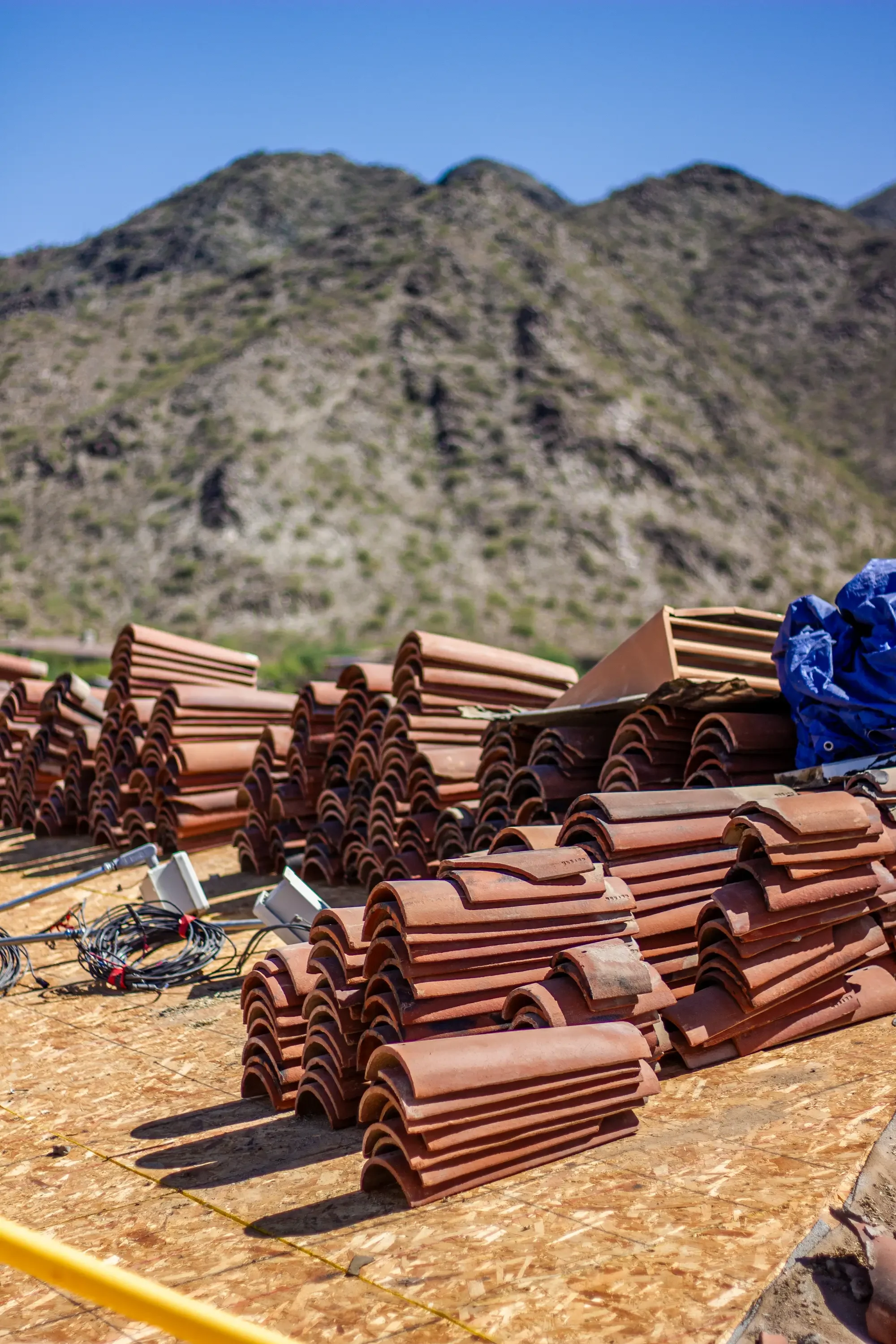 Stacked terracotta clay barrel roof tiles organized in rows on prepared ground with desert mountain backdrop