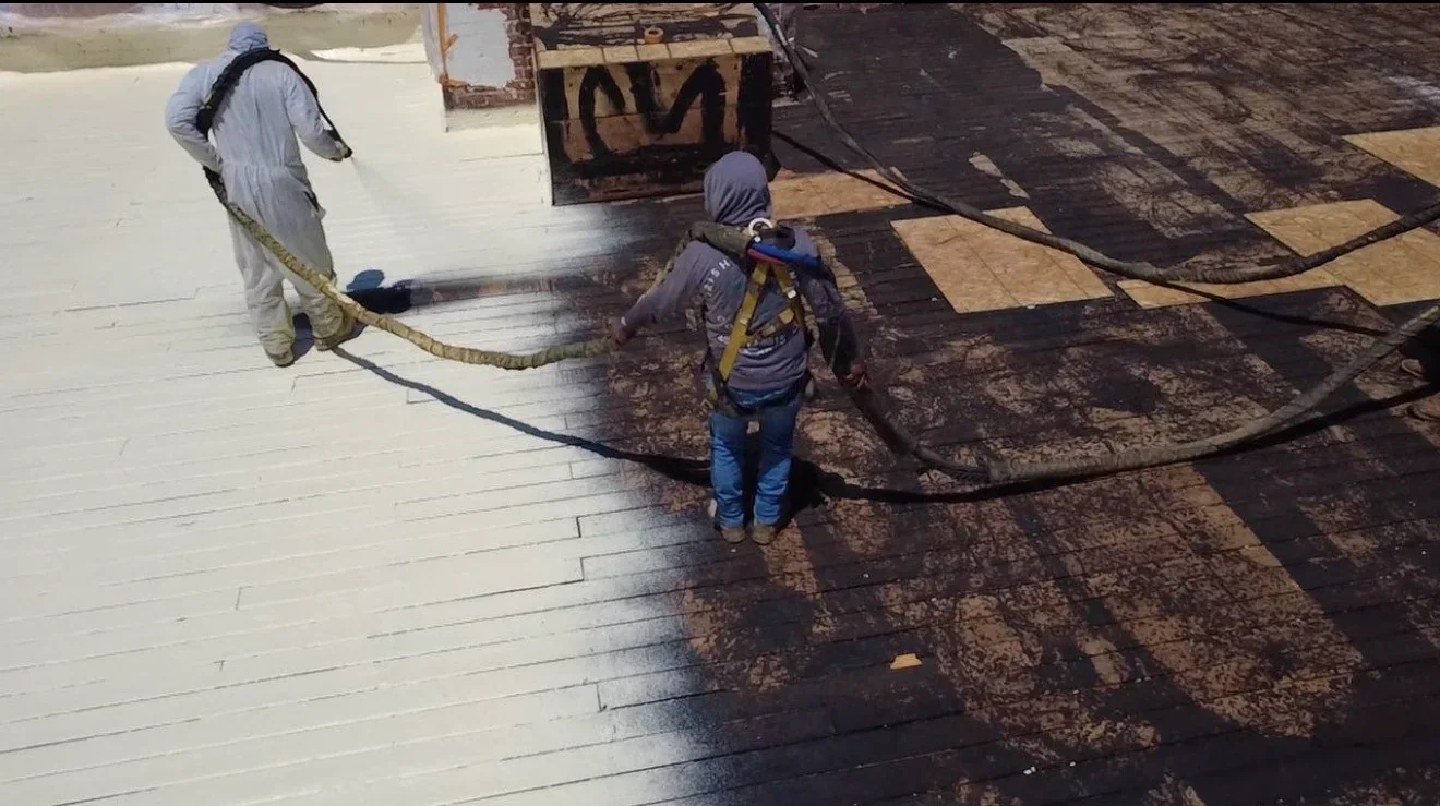 Workers spray-applying waterproof membrane to flat roof with professional equipment
