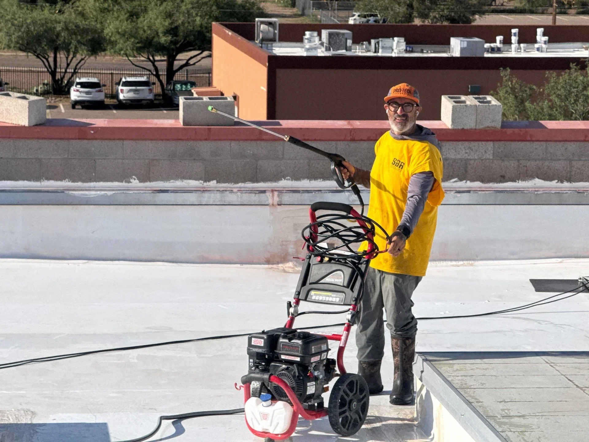 Technician pressure washing commercial flat roof with industrial equipment