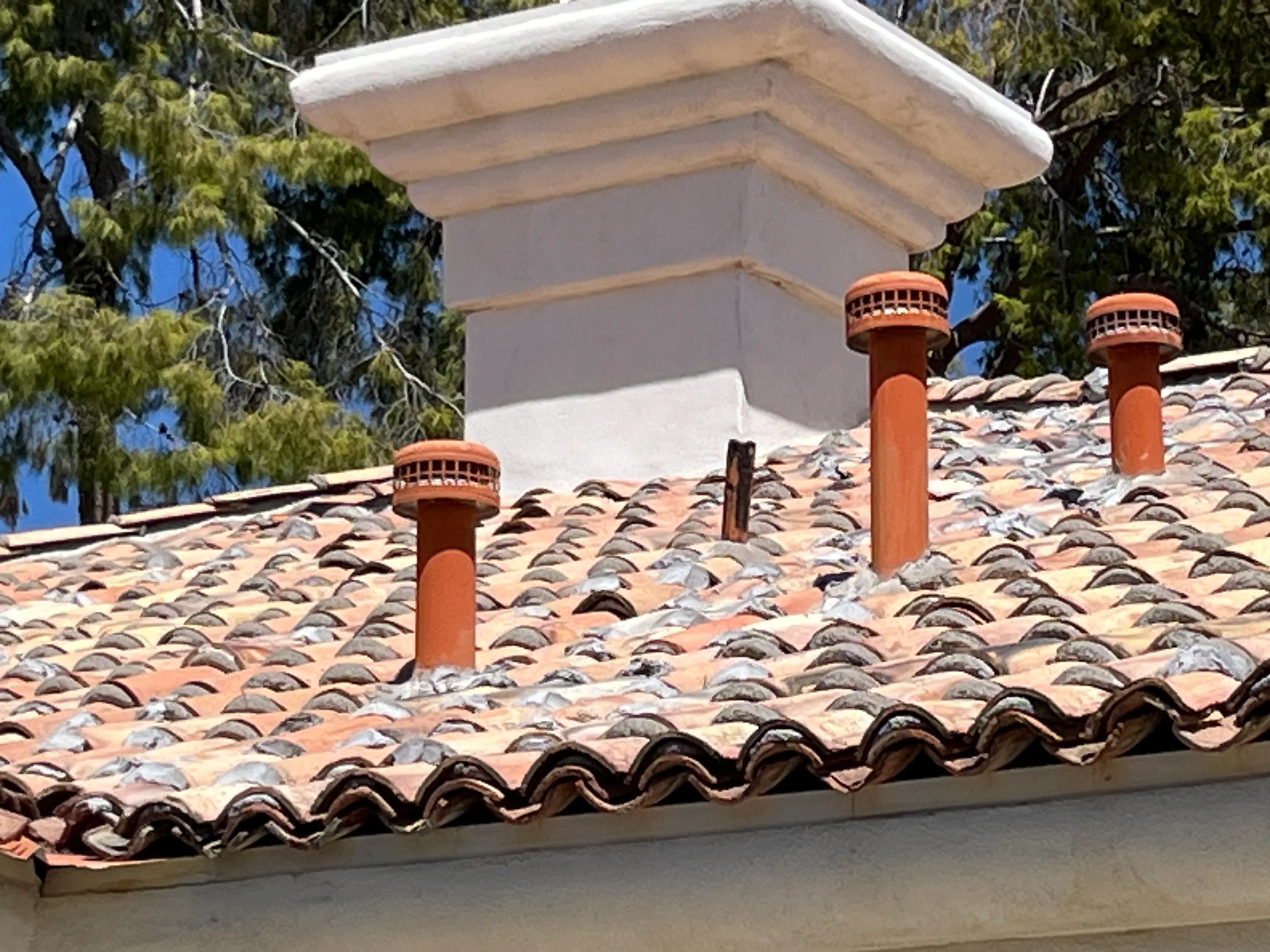 Spanish clay tile roof with three terra cotta chimneys and white fascia trim