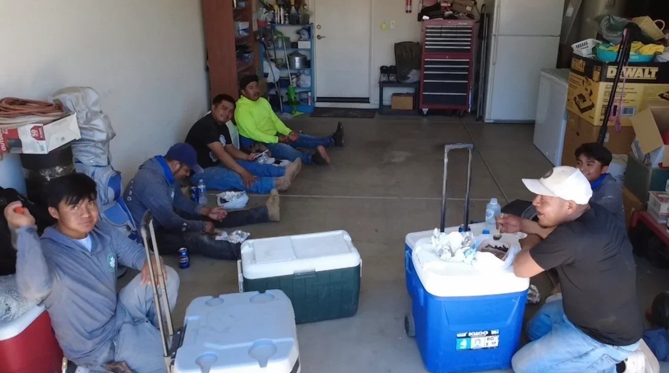 Roofing crew team meeting in workshop with coolers and equipment visible