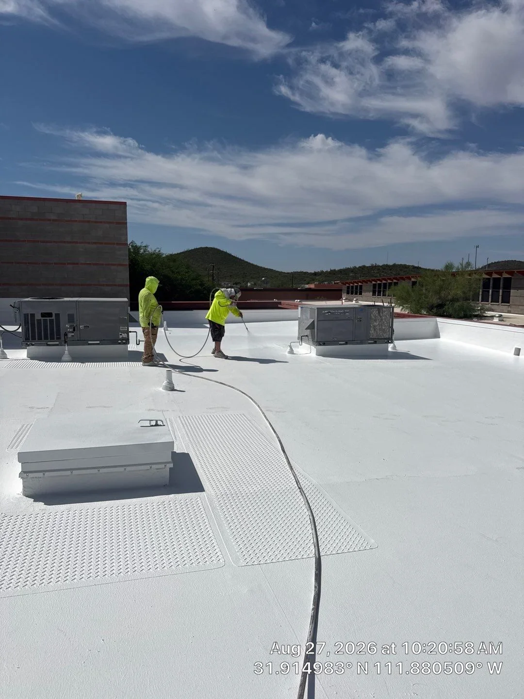 Workers spray white coating on flat roof with walkway pads and HVAC units