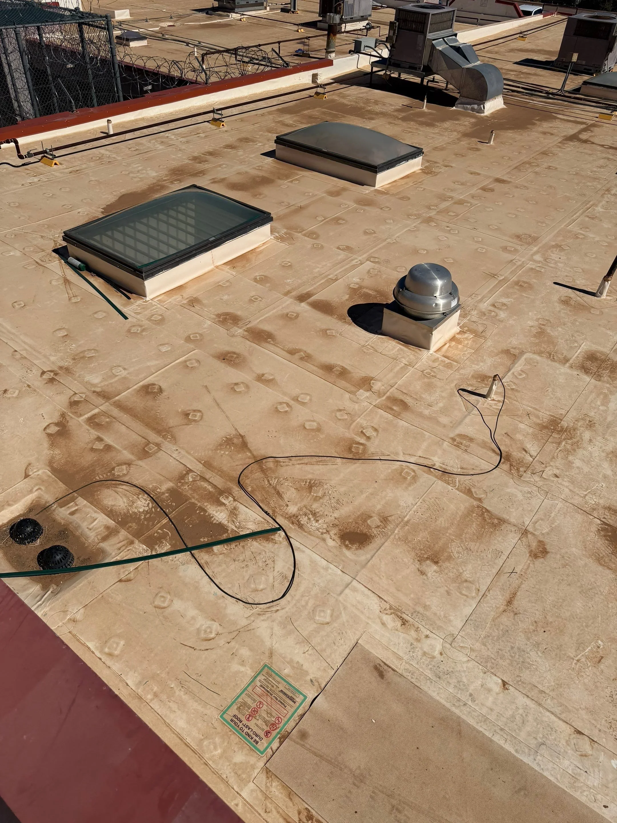 Flat roof with tan membrane, skylight wells, dome vent cap, and electrical conduit