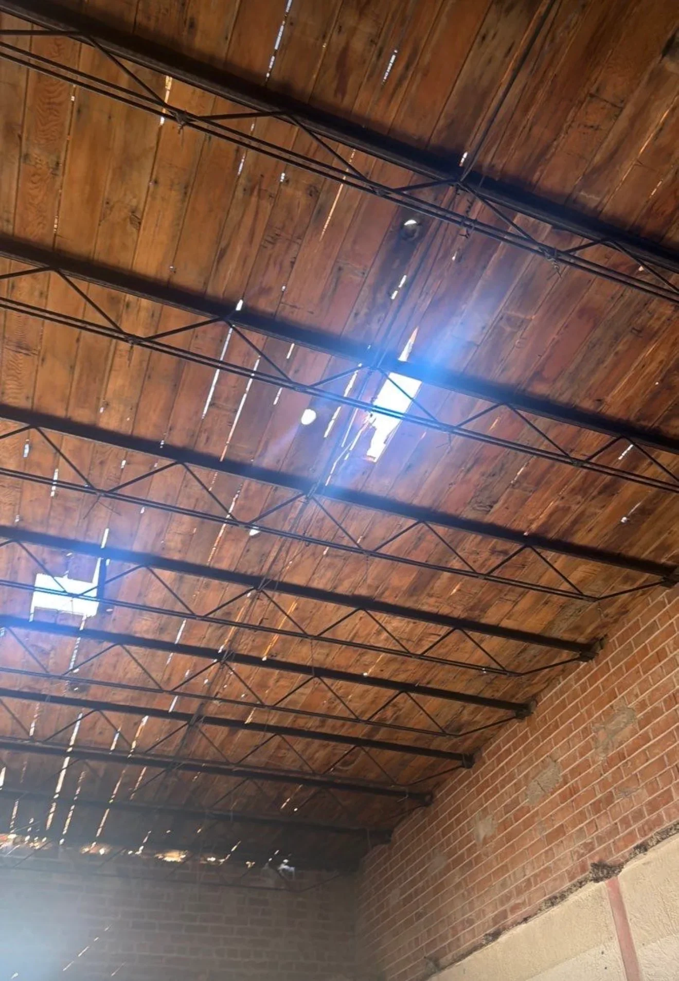 Wooden beam ceiling with steel trusses, recessed lighting, and electrical conduit under brick walls
