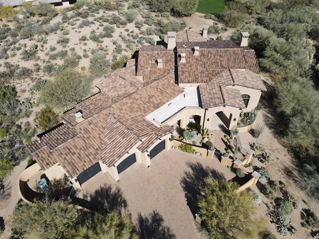 Aerial view of residential roof with brown dimensional shingles, white trim, and stucco walls on desert landscape