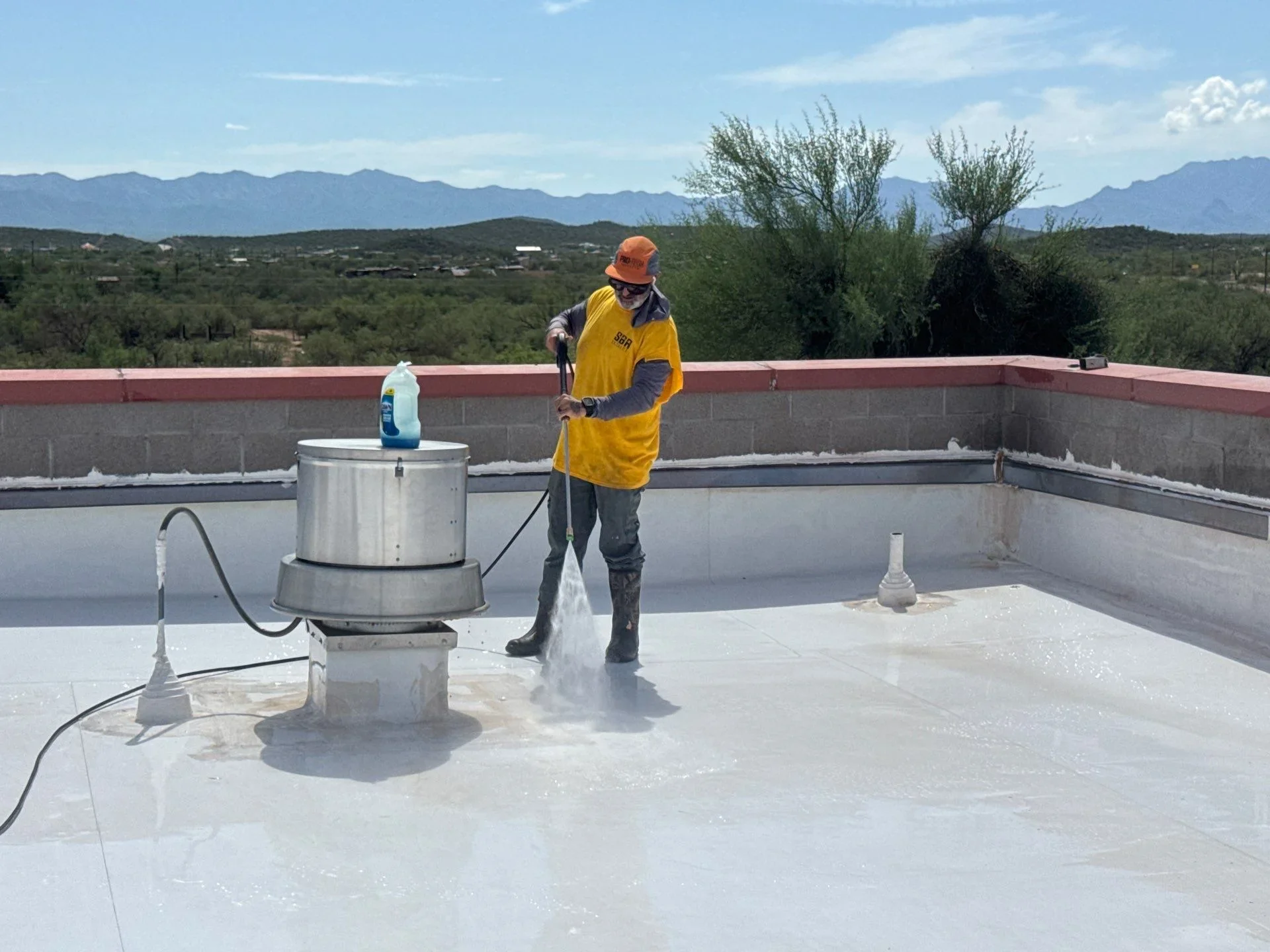Worker applying liquid waterproofing coating to flat roof with spray equipment