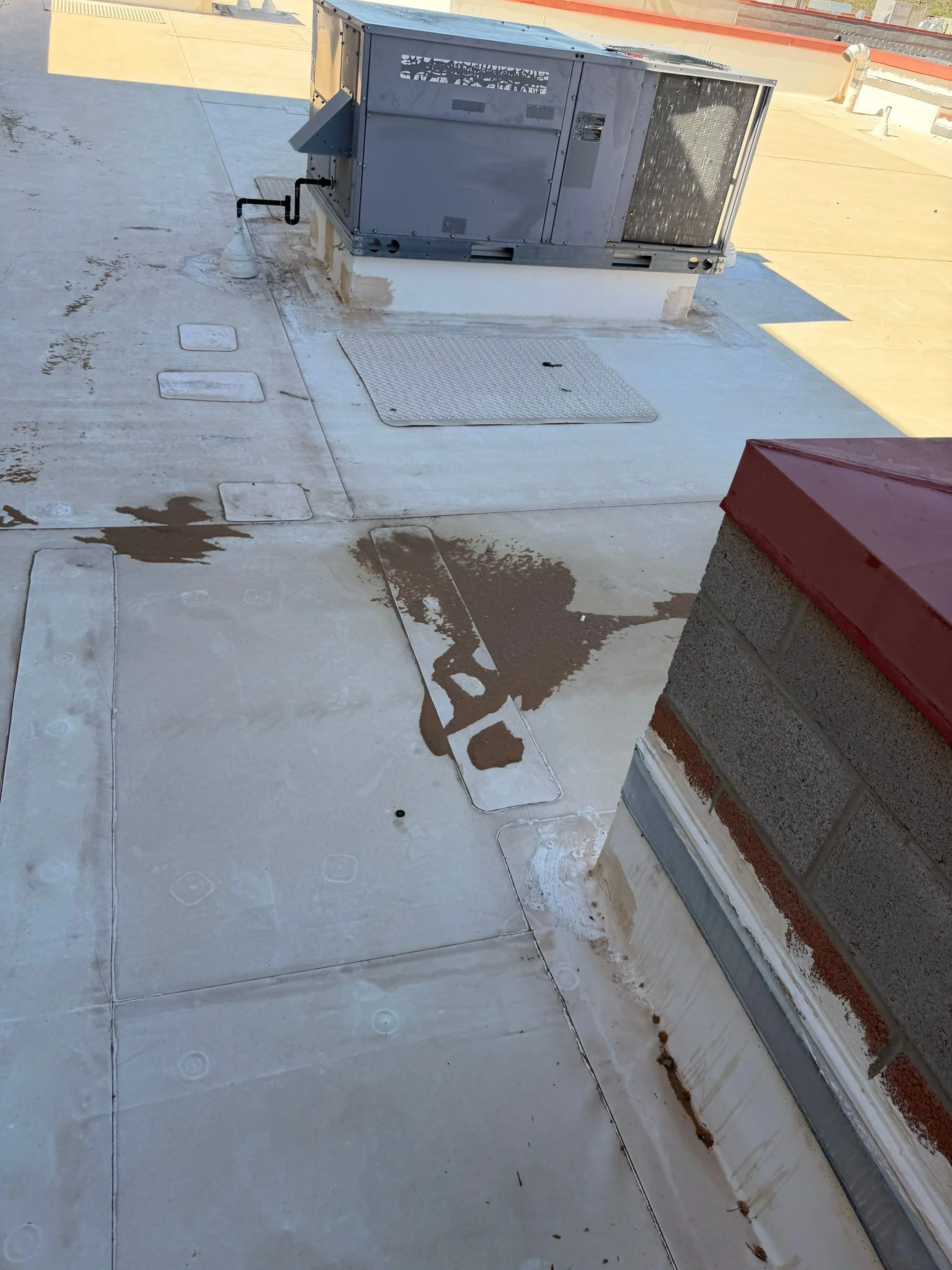 Flat commercial roof with water stains, debris, and HVAC unit during inspection and repair work