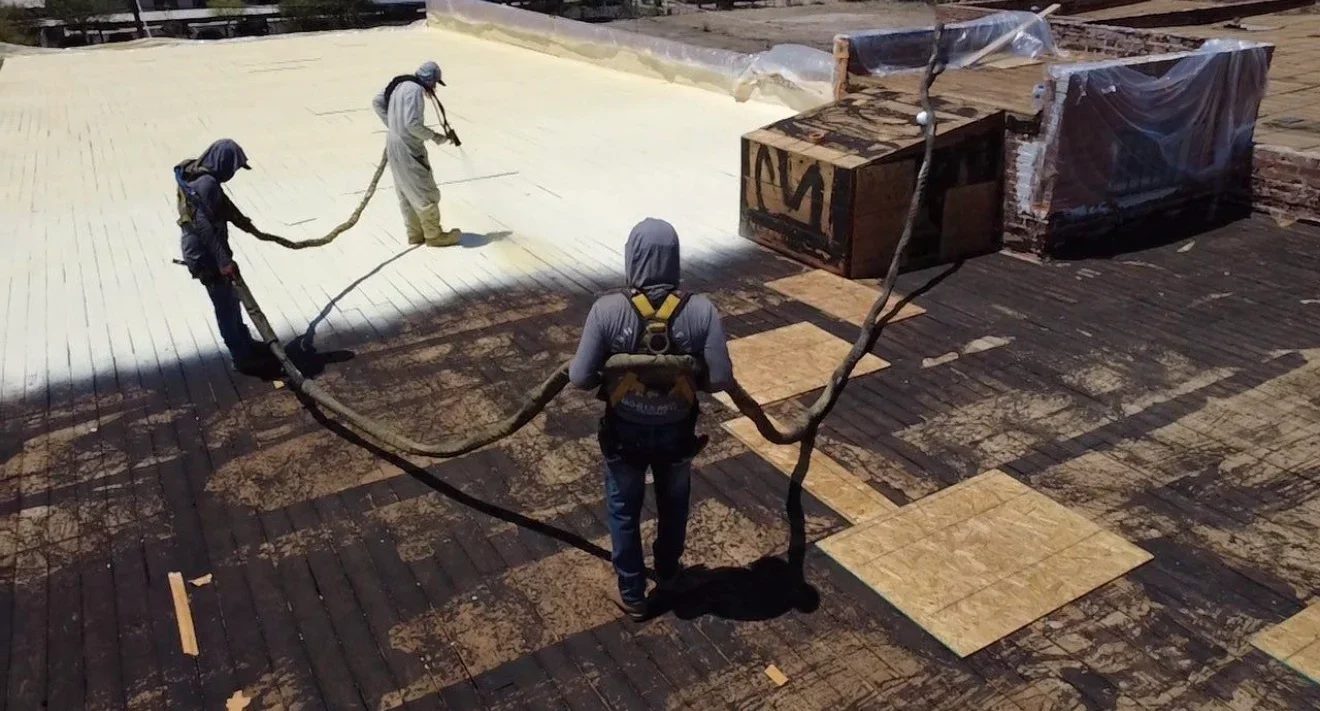 Workers spray-applying white roof coating to commercial flat roof with protective equipment