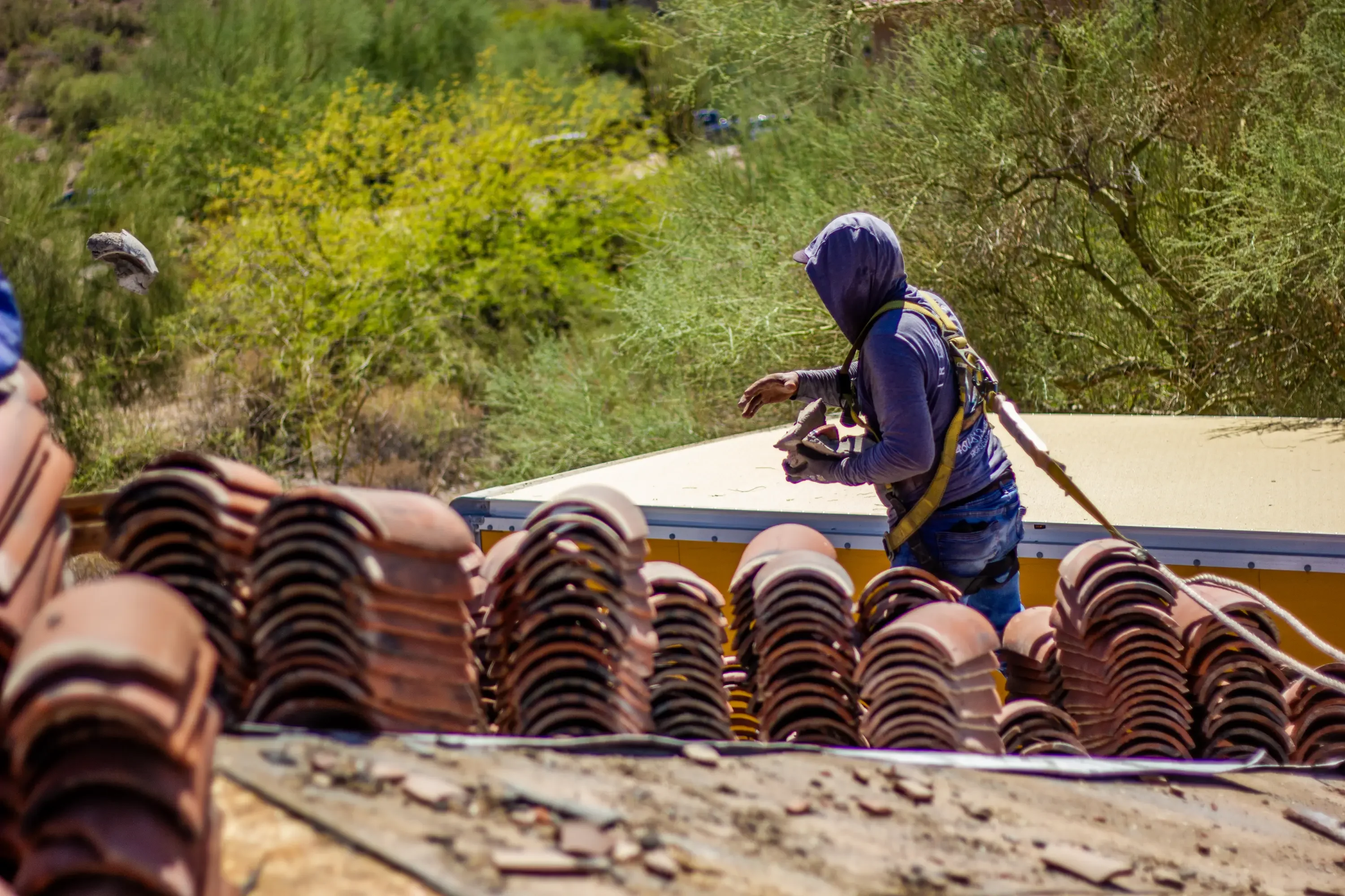 Worker installing clay barrel roof tiles on residential roof with yellow metal underlayment