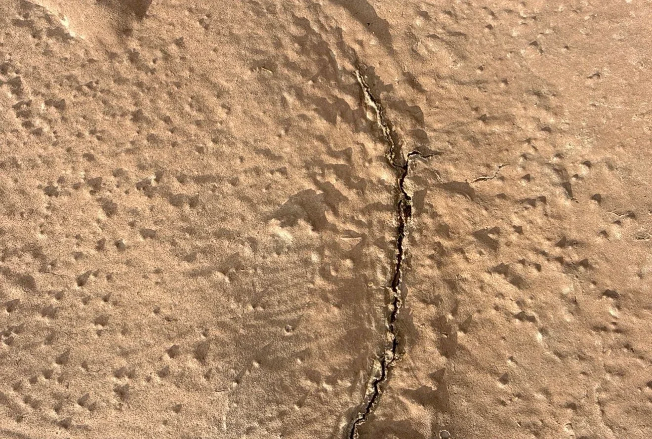 Sealed concrete roof crack with dark caulk on textured concrete surface
