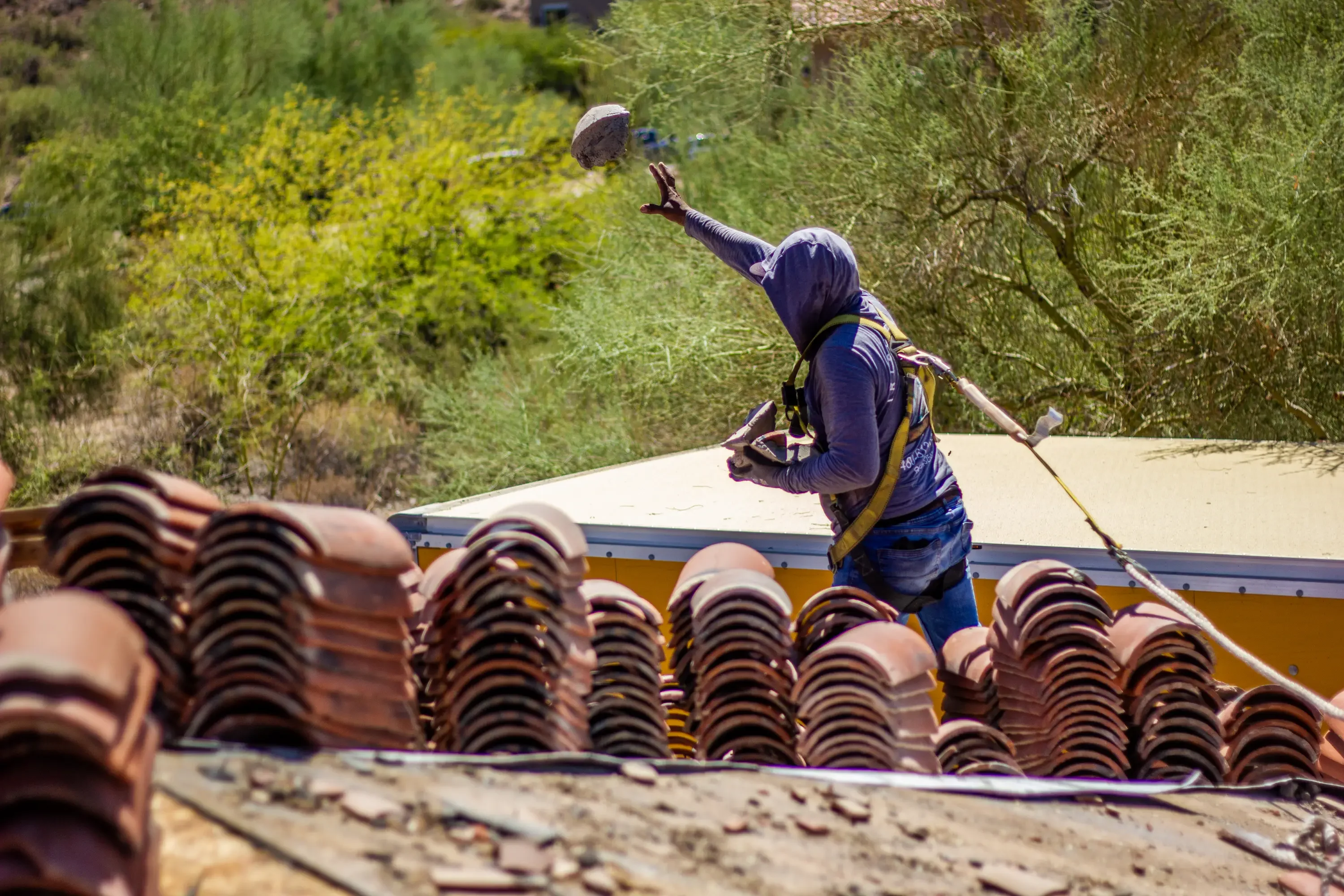Roofer installing Spanish clay barrel tiles on residential roof with organized tile staging below