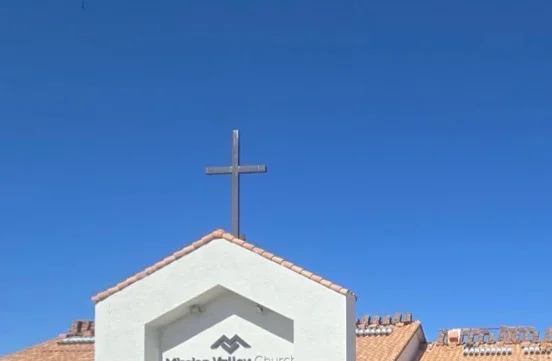 Clay tile pitched roof with decorative ridge and metal cross on white-walled church structure