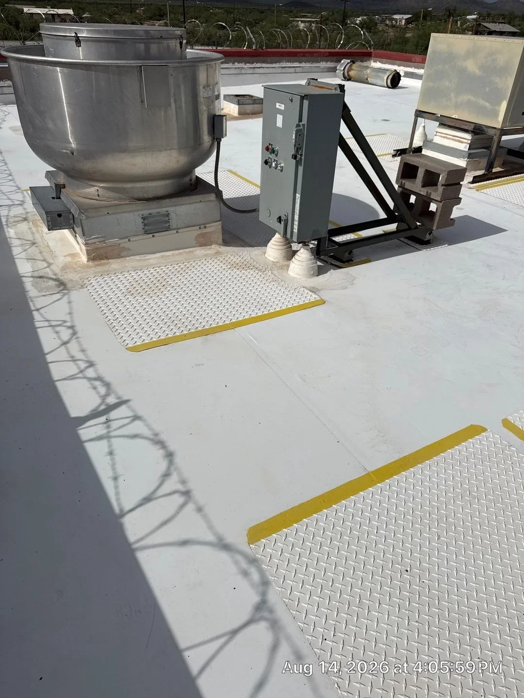 Commercial rooftop with stainless steel HVAC tank, electrical panel, and yellow-striped aluminum walkway pads on white membrane roof