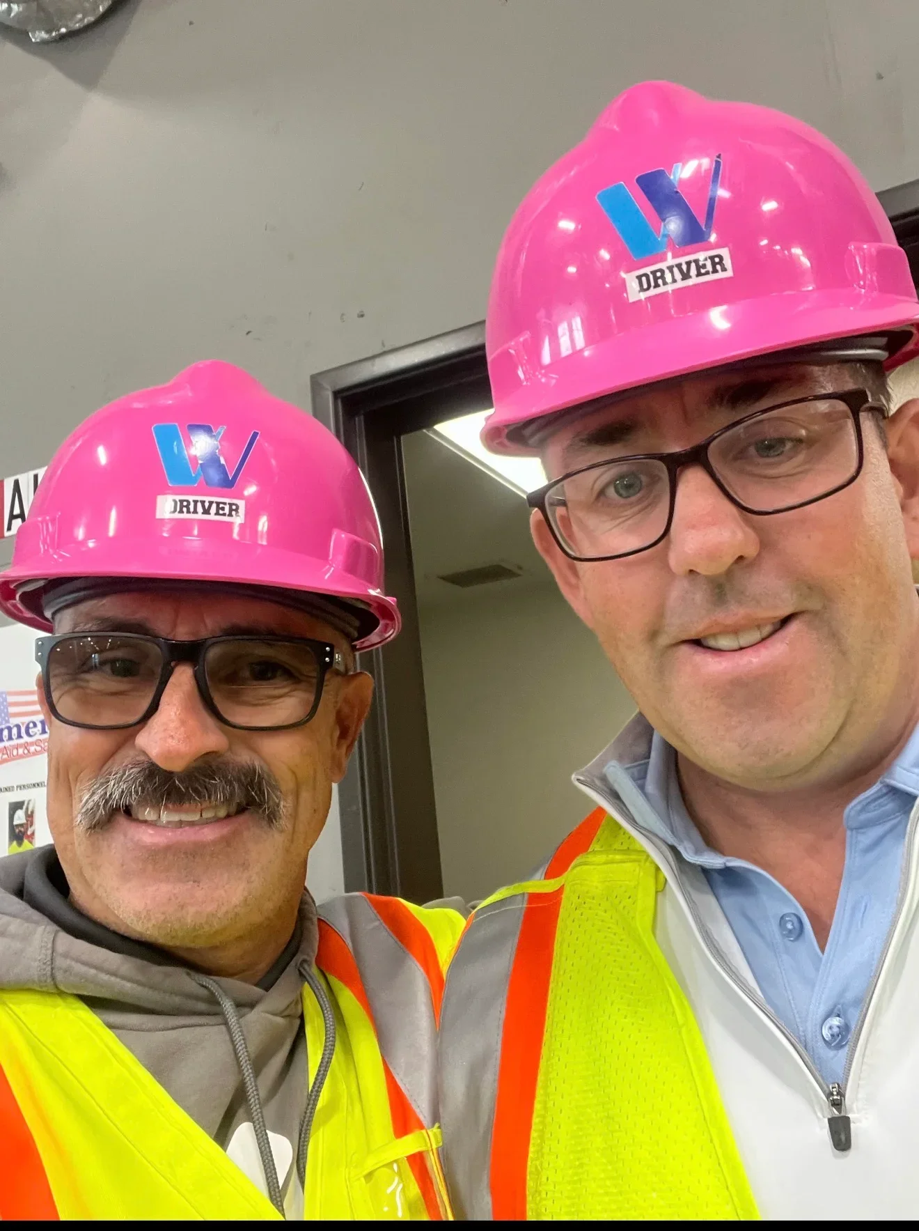 Two workers in neon yellow safety vests and pink hard hats on construction site